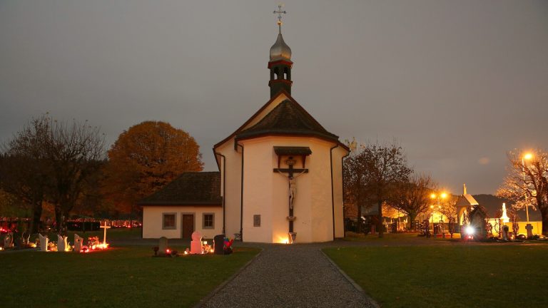 Friedhofskapelle in Einsiedeln am Abend mit brennenden Kerzen an den Gräbern