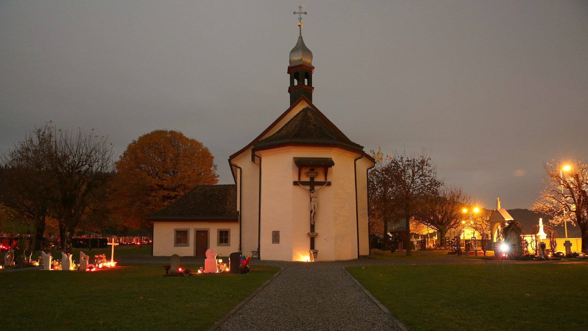 Friedhofskapelle in Einsiedeln am Abend mit brennenden Kerzen an den Gräbern