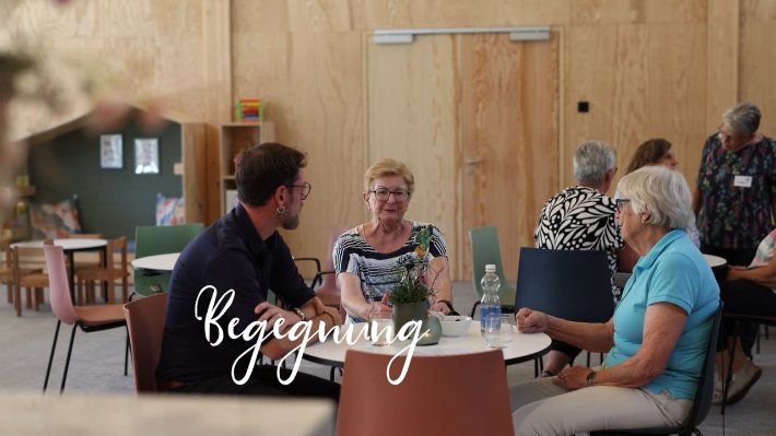 Vorschaubild des Videos: Menschen sitzen im Pfarreiheim zusammen, dazu der Schriftzug Begegnung