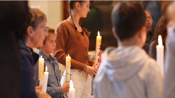 Kinder und Erwachsene stehen in der Kirche und halten brennende Kerzen